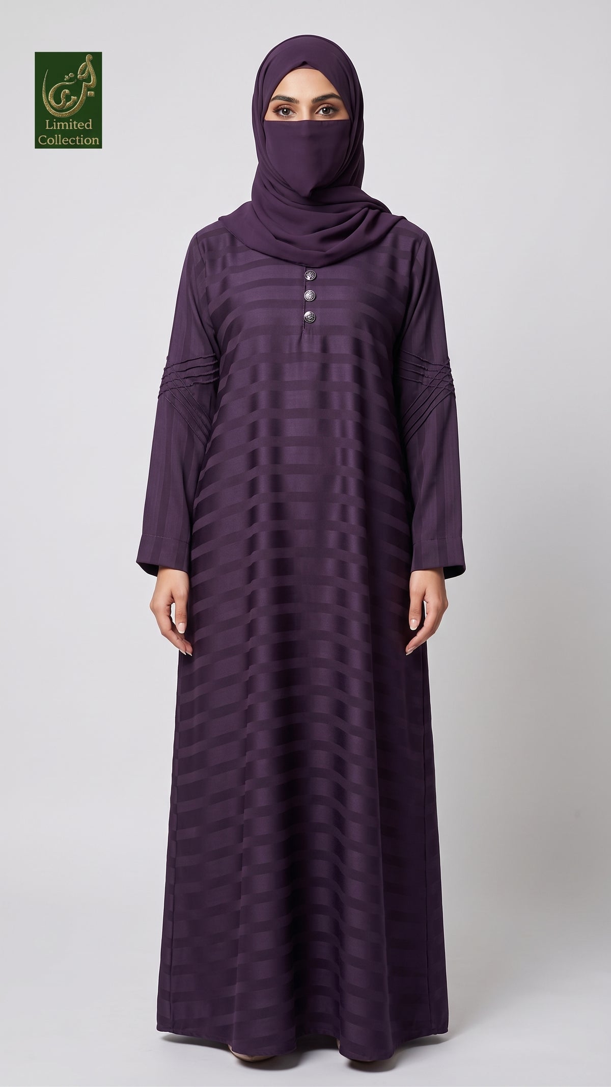 A woman wearing a long, floor-length dark purple abaya with a matching headscarf and face veil, standing against a light gray studio background. The abaya has a subtle horizontal striped texture and a buttoned neckline.