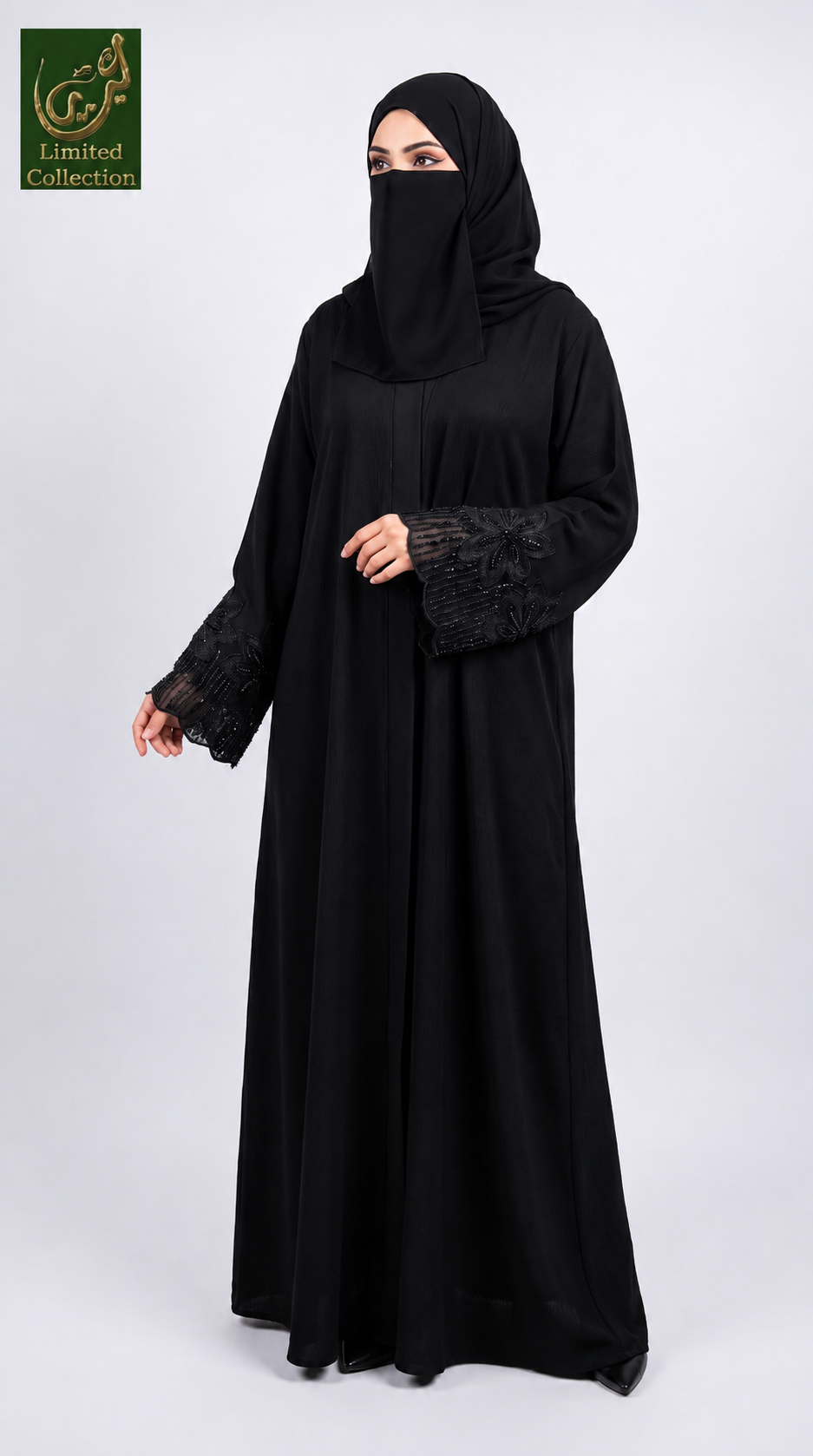 A woman wearing a full-length black abaya with stonework lace embroidered sleeves and a matching black hijab, standing against a light gray studio background. A green 'Abayat Limited Collection' logo appears in the top-left corner.