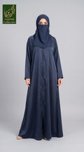 A woman wearing a long navy blue abaya and matching hijab stands against a light gray studio background. A green 'Abayat Limited Collection' logo appears in the top-left corner.