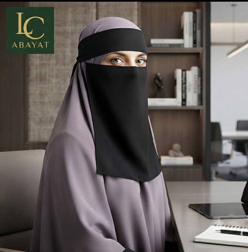 A woman wearing a modest head covering in a muted dusty lavender and black, seated at a desk in an office environment. The brand logo 'LC ABAYAT' is visible in the top-left corner.