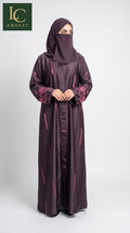 A woman wearing a long dark plum Geometric Printed Jacquard Front Open Abaya with pink floral embroidery on the sleeves and pink vertical line patterns, paired with a matching face-covering hijab. The image features an 'LC ABAYAT' brand logo in the top-left corner against a light gray studio background.