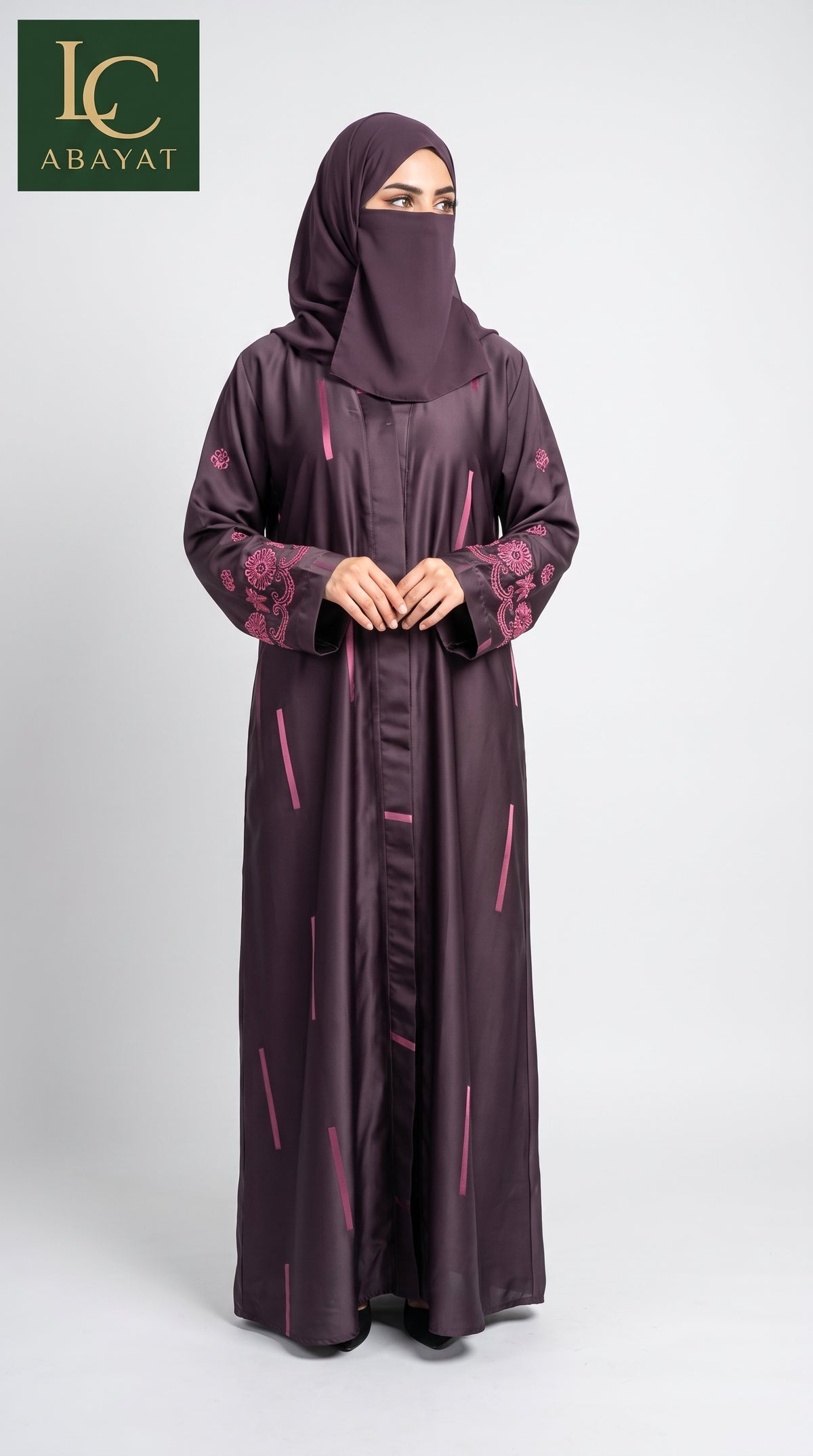 A woman wearing a long dark plum Geometric Printed Jacquard Front Open Abaya with pink floral embroidery on the sleeves and pink vertical line patterns, paired with a matching face-covering hijab. The image features an 'LC ABAYAT' brand logo in the top-left corner against a light gray studio background.