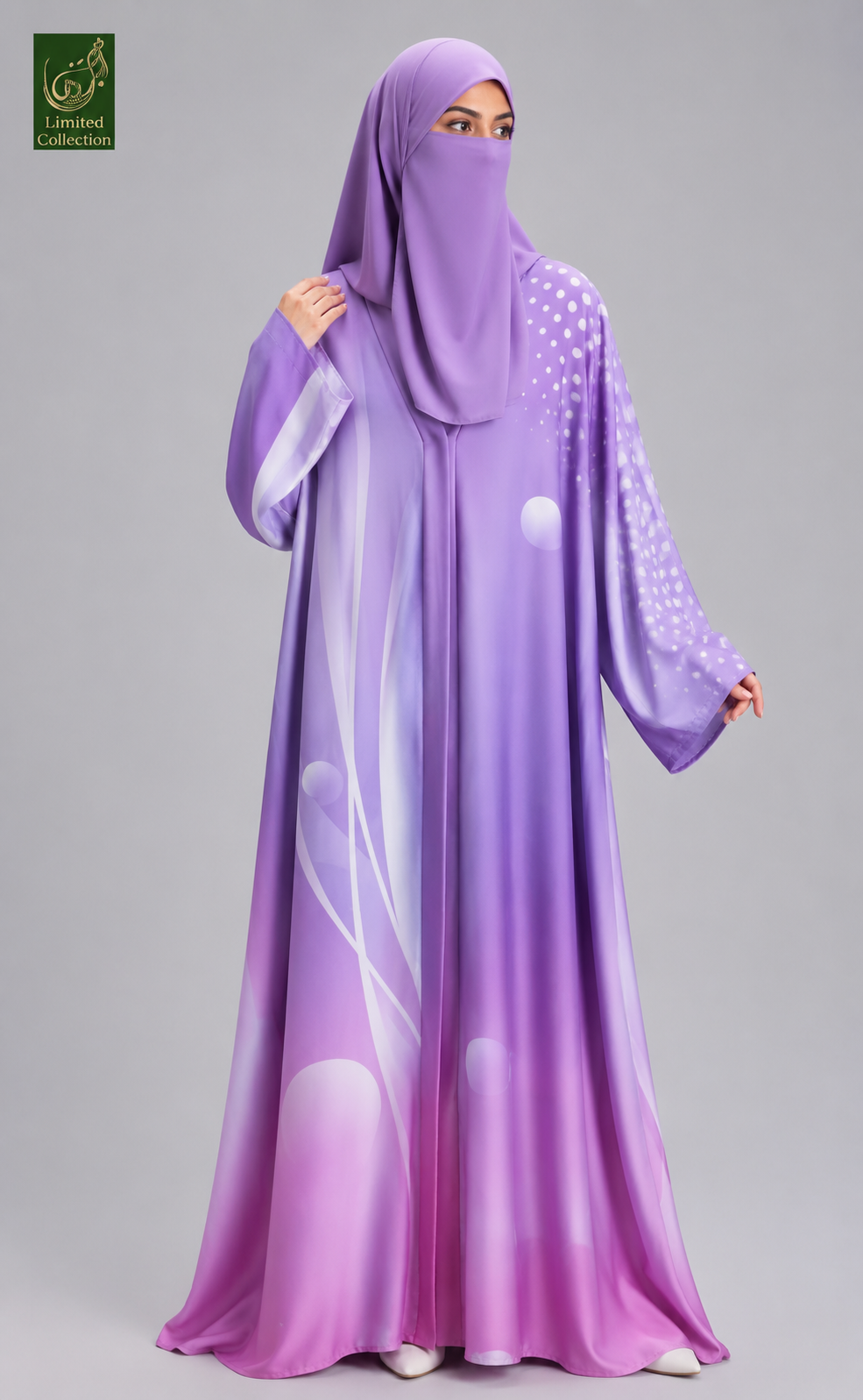 A woman wearing a flowing purple abaya and matching hijab with white abstract and dotted patterns, photographed against a plain light gray studio background. A small green logo appears in the top-left corner.