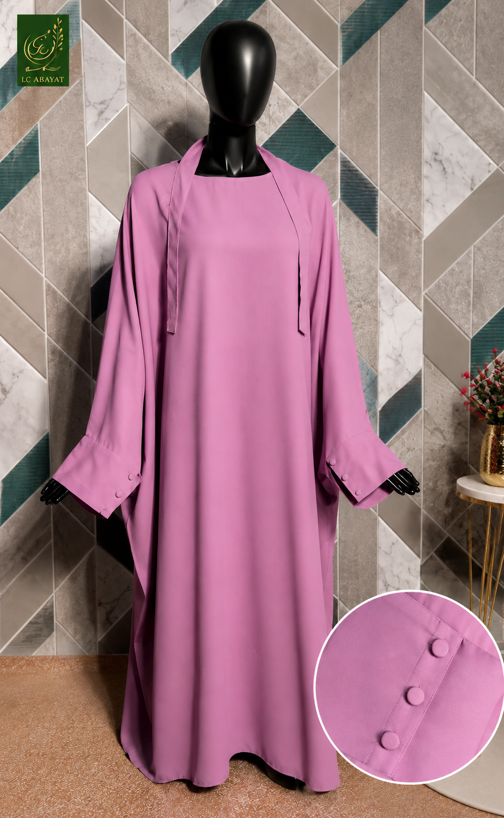 A long-sleeved Jilbab in dusty pink is displayed on a black mannequin. The dress features a high neckline, a straight silhouette, and wide sleeves with button details at the cuffs.