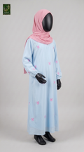 A child's long light blue abaya with small pink bow prints, styled with a pink hijab on a black mannequin against a light gray studio background.