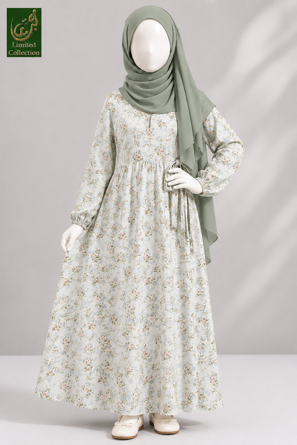 A long-sleeved maxi abaya for kids with a delicate beige and green floral pattern, styled on a mannequin with a sage green hijab. The image is from the 'Limited Collection' line, shown against a neutral gray background with soft shadows.