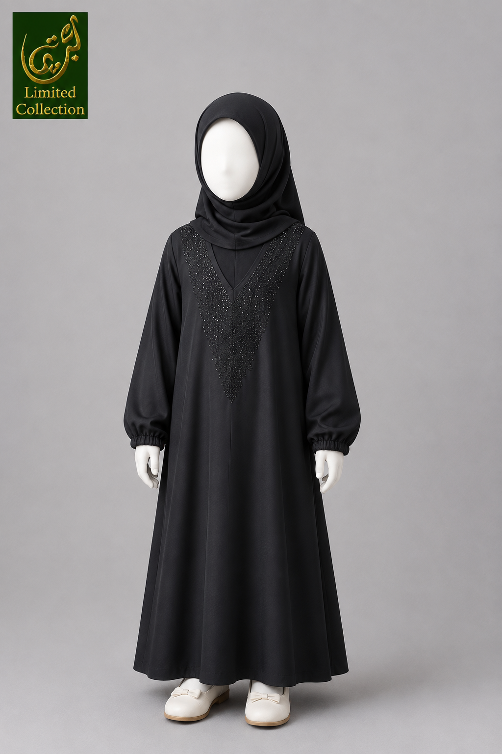 A black long-sleeved abaya dress with embroidered detailing on the chest, styled on a mannequin kid with a matching black hijab, white gloves, and white shoes against a solid gray background. A 'Limited Collection' logo is visible in the top-left corner.