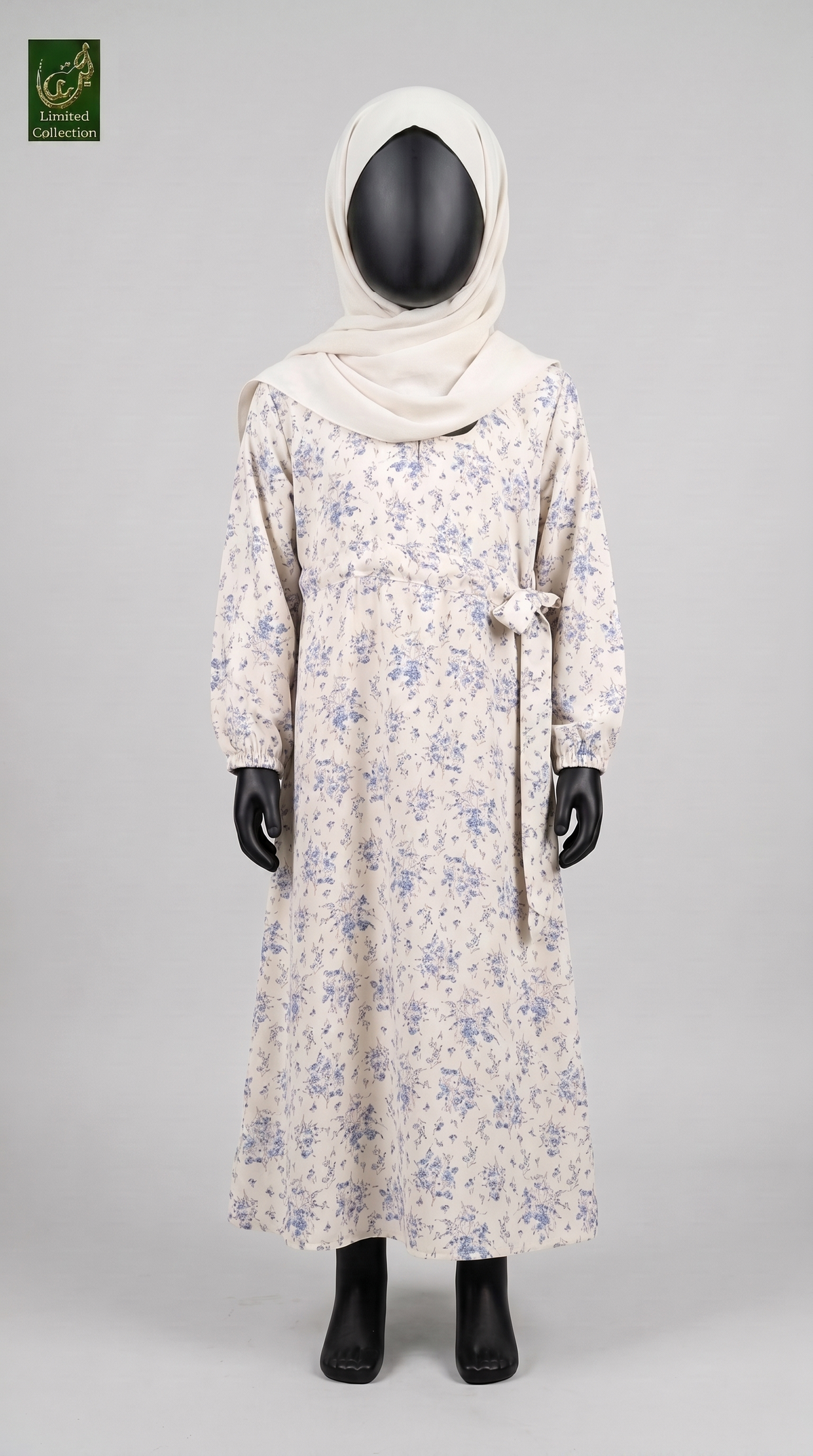 A long-sleeve modest abaya with a blue floral print on a cream base, styled on a black mannequin with a cream hijab. The image is set against a solid light gray background.