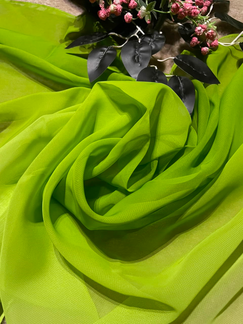 Bright lime green sheer mesh fabric draped in soft folds, with a small decorative floral arrangement placed at the top edge.