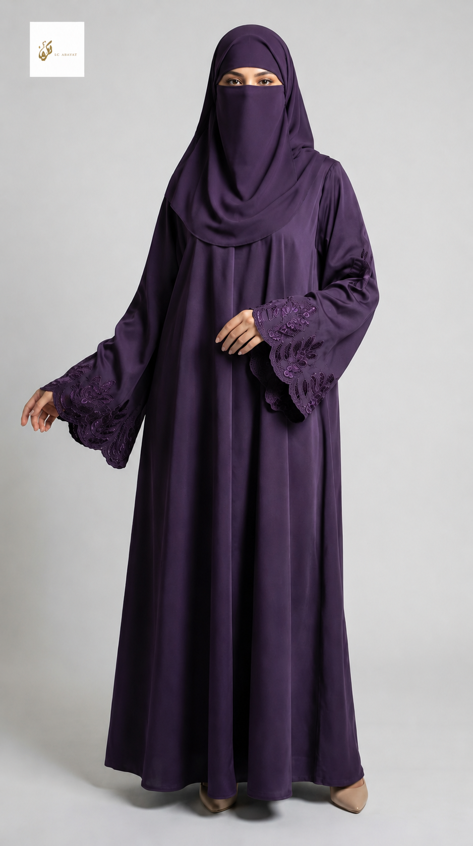 A woman wearing a long, flowing deep purple abaya with matching head covering and a face veil, standing against a light gray studio background.