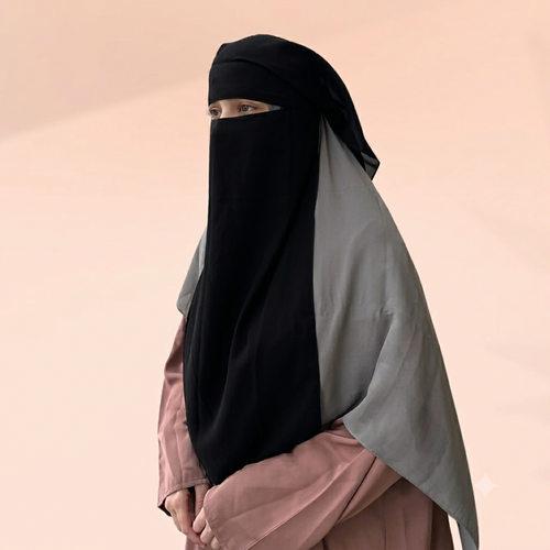 A woman wearing a black niqab and a light gray hijab, paired with a dusty rose abaya, set against a solid pale peach background.