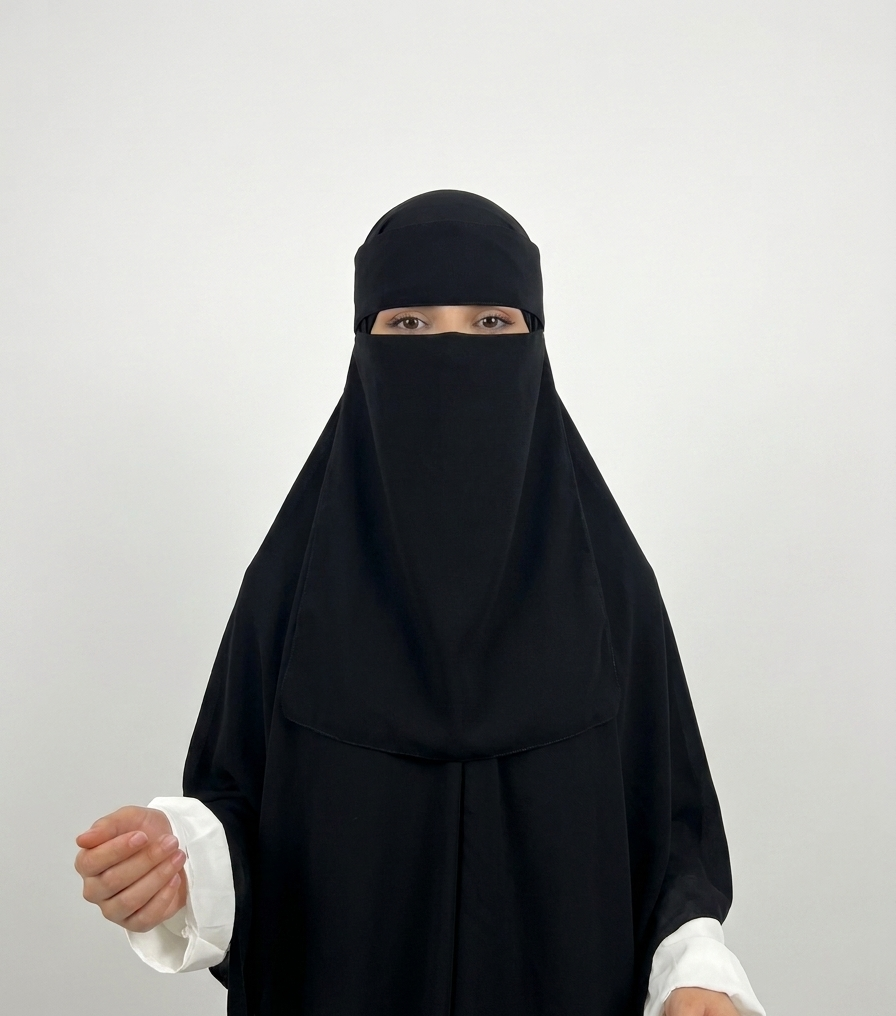 A woman wearing a black full-body modest garment with a face-covering veil and white sleeve cuffs, photographed against a plain light gray studio background.
