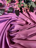 Purple draped fabric with pink flowers and dark leaves arranged on top, photographed in a styled flat-lay composition.