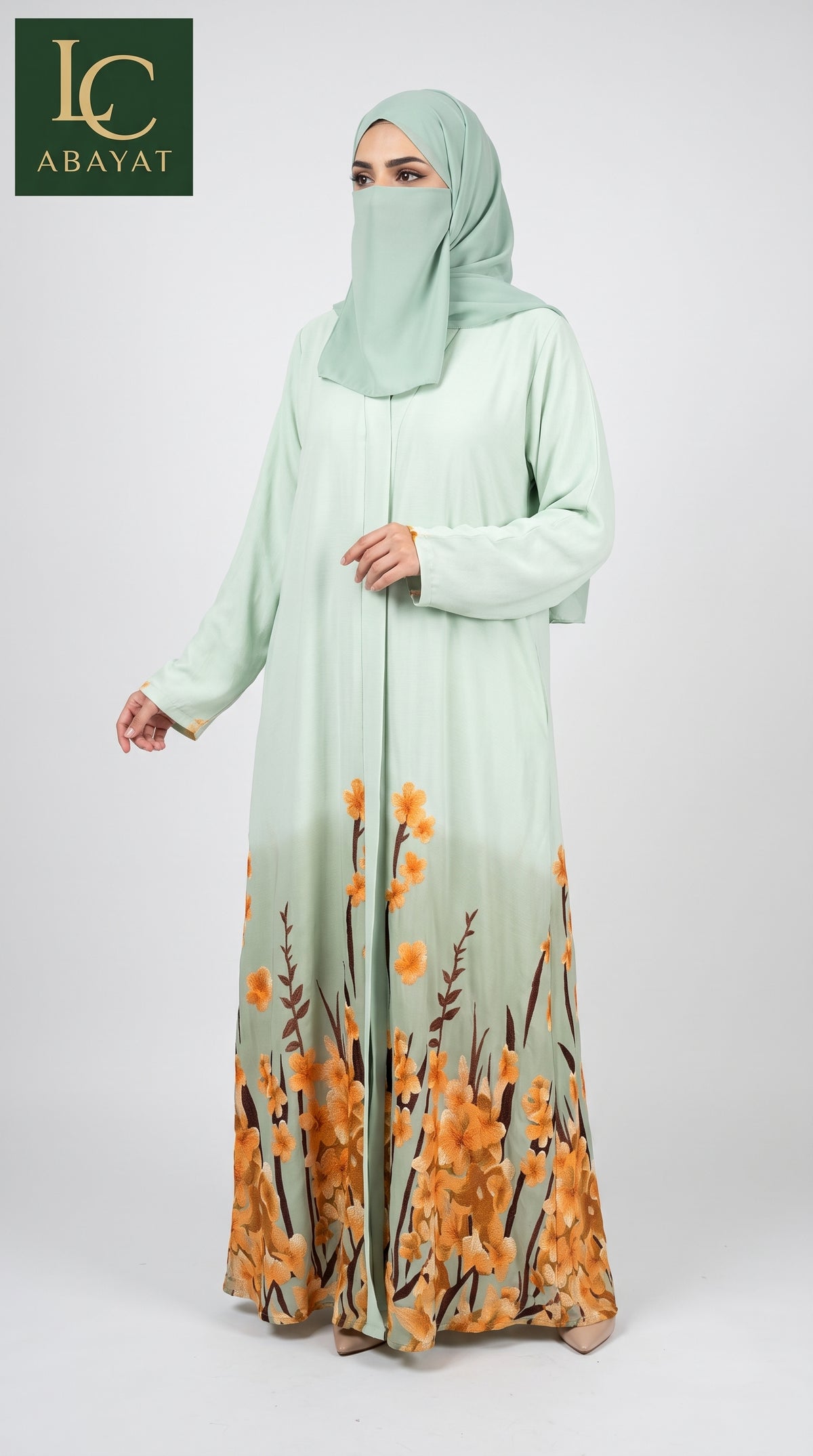 A woman modeling a mint green long-sleeved front-open abaya with a matching hijab. The abaya features a gradient transition at the hem transitioning to an orange and brown floral print.