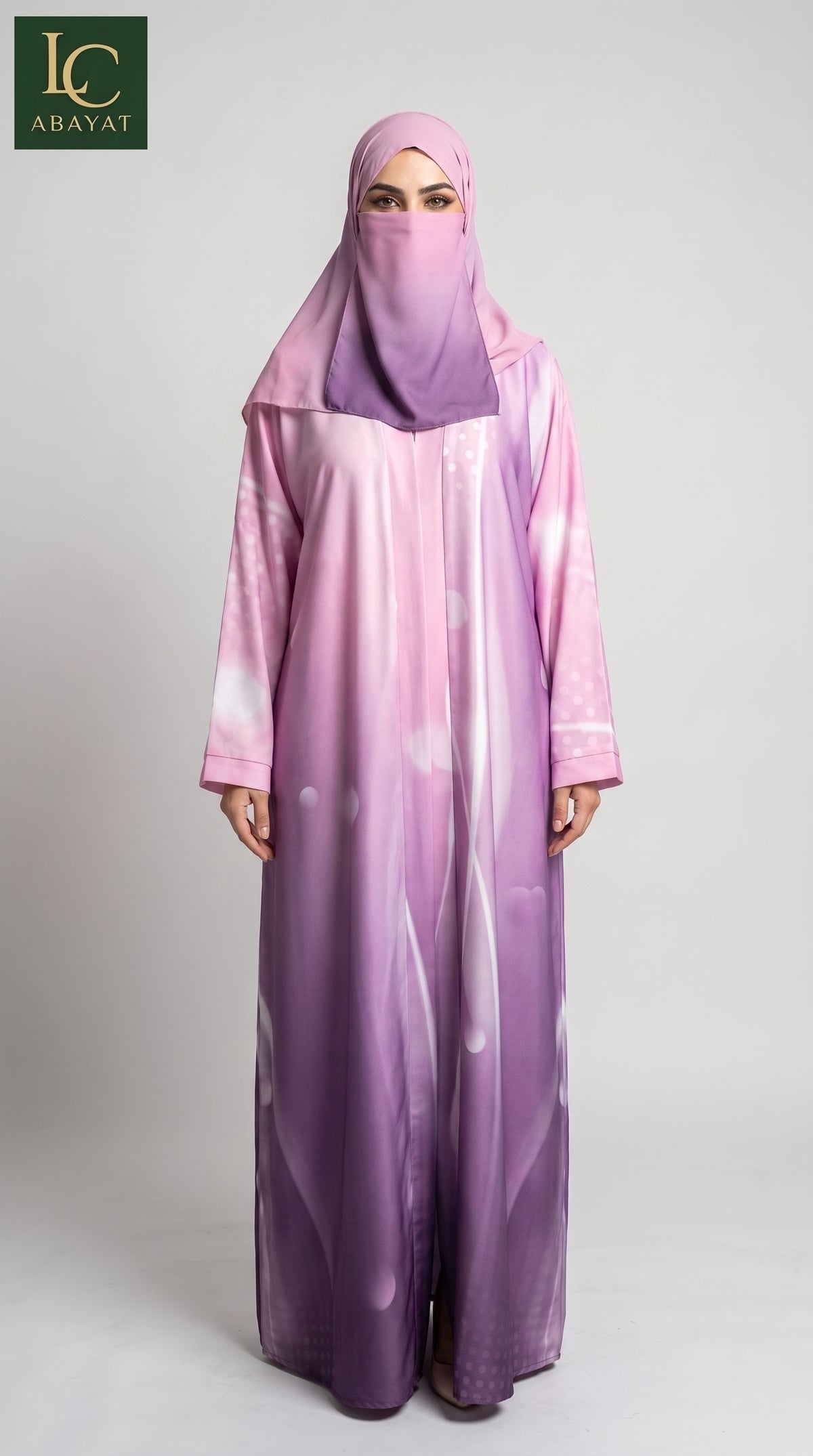 A woman wearing a long, wide-sleeved abaya in a pink-to-purple ombré gradient with a matching purple hijab, standing against a light gray studio background. The LC Abaya brand logo is visible in the top-left corner.