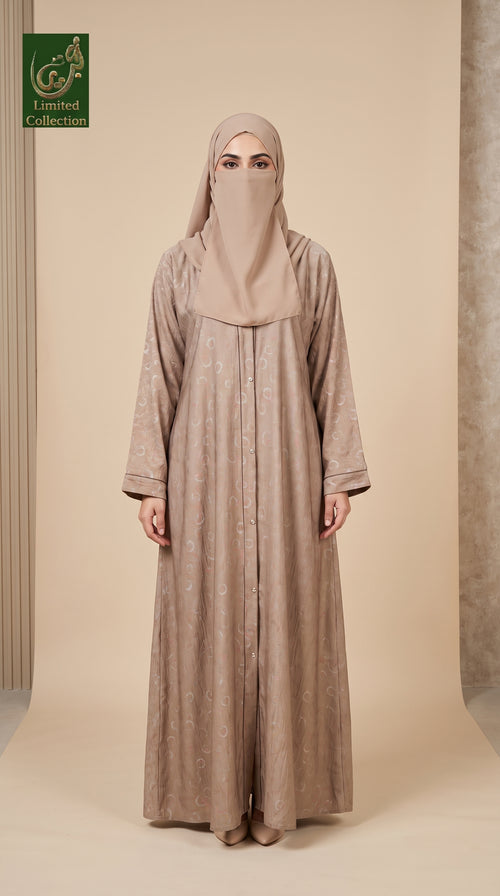 A woman wearing a long beige abaya with a matching hijab and face veil, standing against a neutral beige studio backdrop. The abaya has a subtle tonal pattern and wide sleeves.