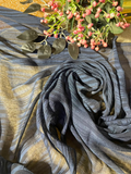 A draped piece of textured fabric in slate blue and beige stripes, styled with a decorative floral sprig on a warm wooden surface.
