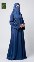 A woman wearing a long, flowing navy blue abaya with matching hijab and embroidered sleeves, standing against a light gray studio background. A green 'Limited Collection' logo is visible in the top-left corner.