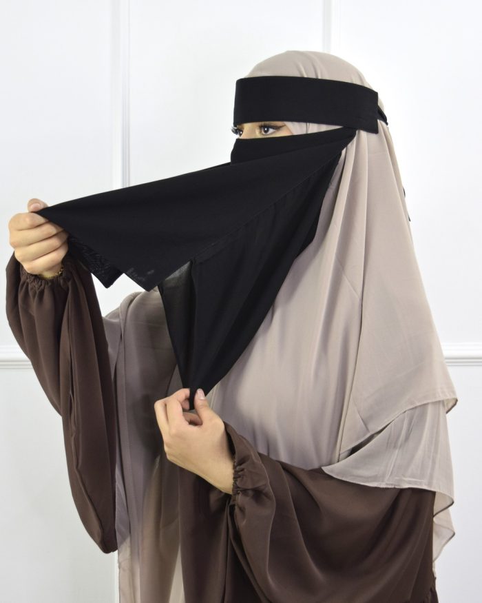 Person wearing a brown outfit with a black and beige veil against a white background