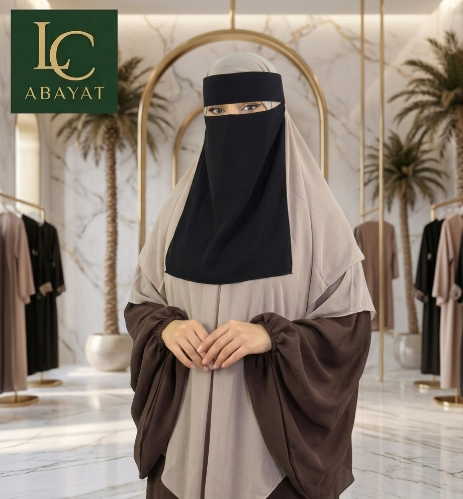 A woman wearing a modest outfit with a black face veil and a draped two-tone abaya in beige and brown, standing in a luxury boutique with marble floors and gold arches. The 'LC ABAYAT' logo is visible in the top-left corner.