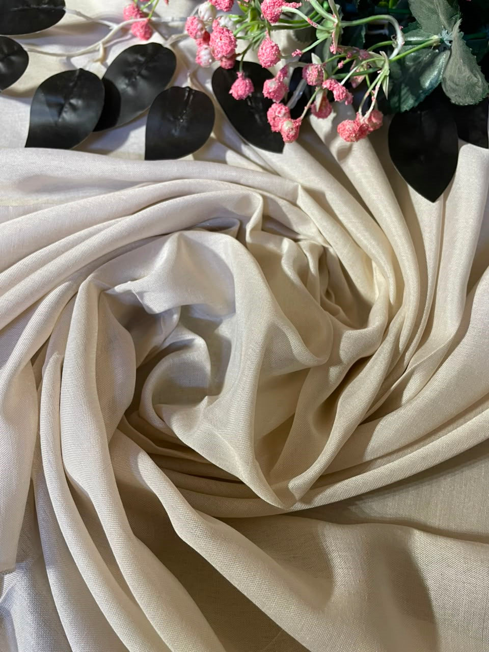Cream-colored fabric draped in elegant swirls, styled with black leaves and pink berries at the top edge.
