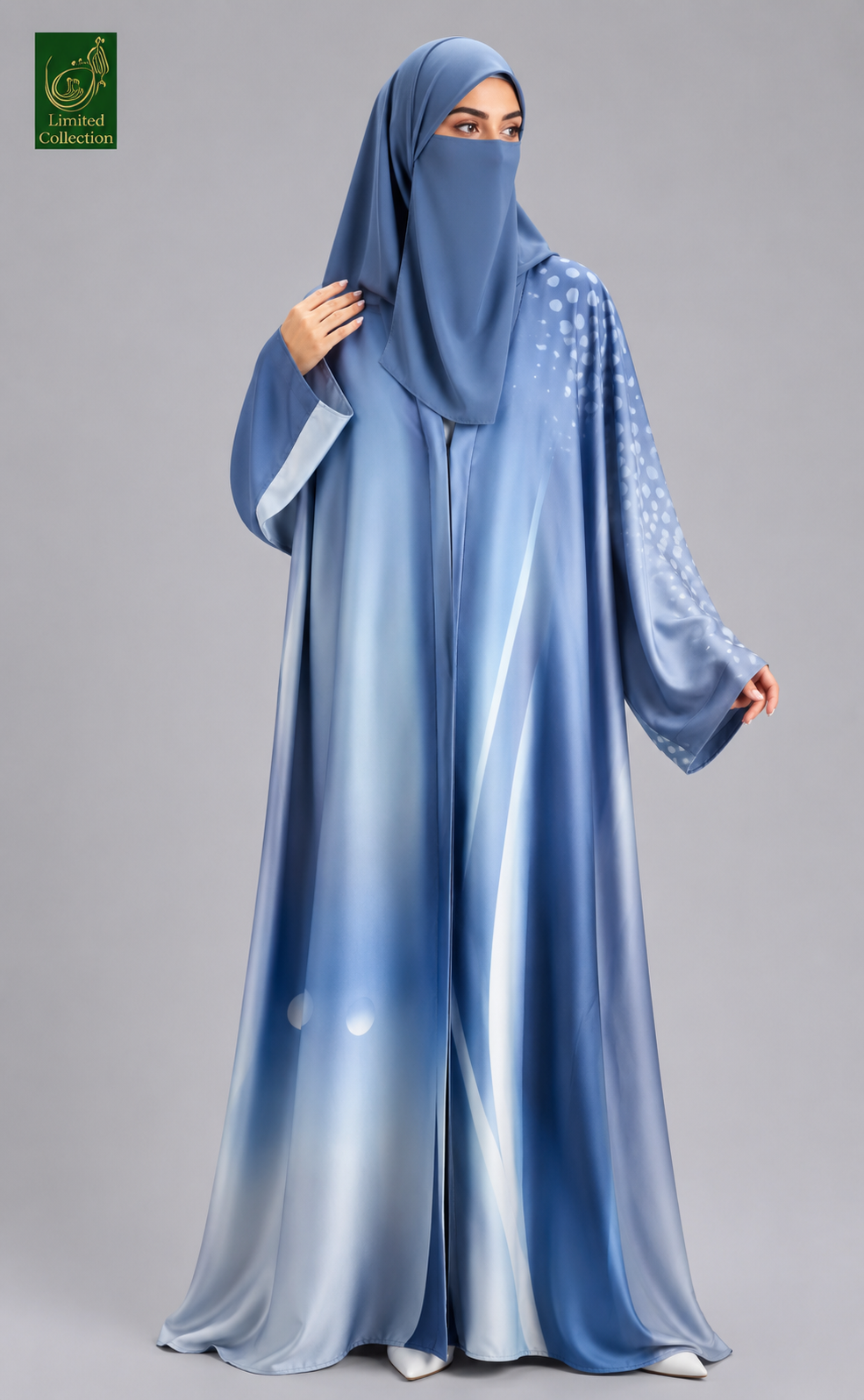 A woman wearing a flowing blue abaya with a matching hijab and face veil, standing against a plain gray studio background. The abaya has a gradient effect from darker blue at the top to lighter blue at the bottom, with subtle white dot patterns on the sleeves.