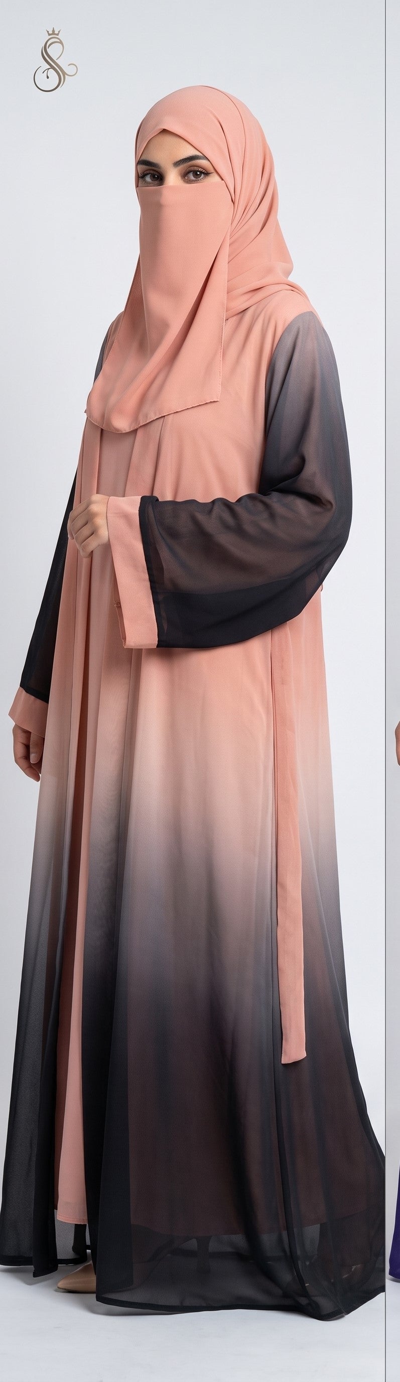 A woman wearing a modest long front open kimono abaya with a peach-pink to black ombre gradient, paired with a matching hijab, shown against a plain light gray studio background.