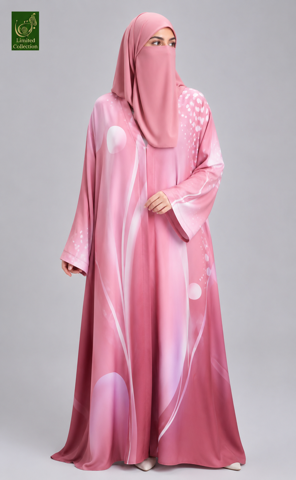 A woman wearing a pink abaya and matching hijab with a subtle abstract white and pink pattern, photographed against a neutral gray studio background. A small green 'Lamb and Collection' logo is visible in the top-left corner.