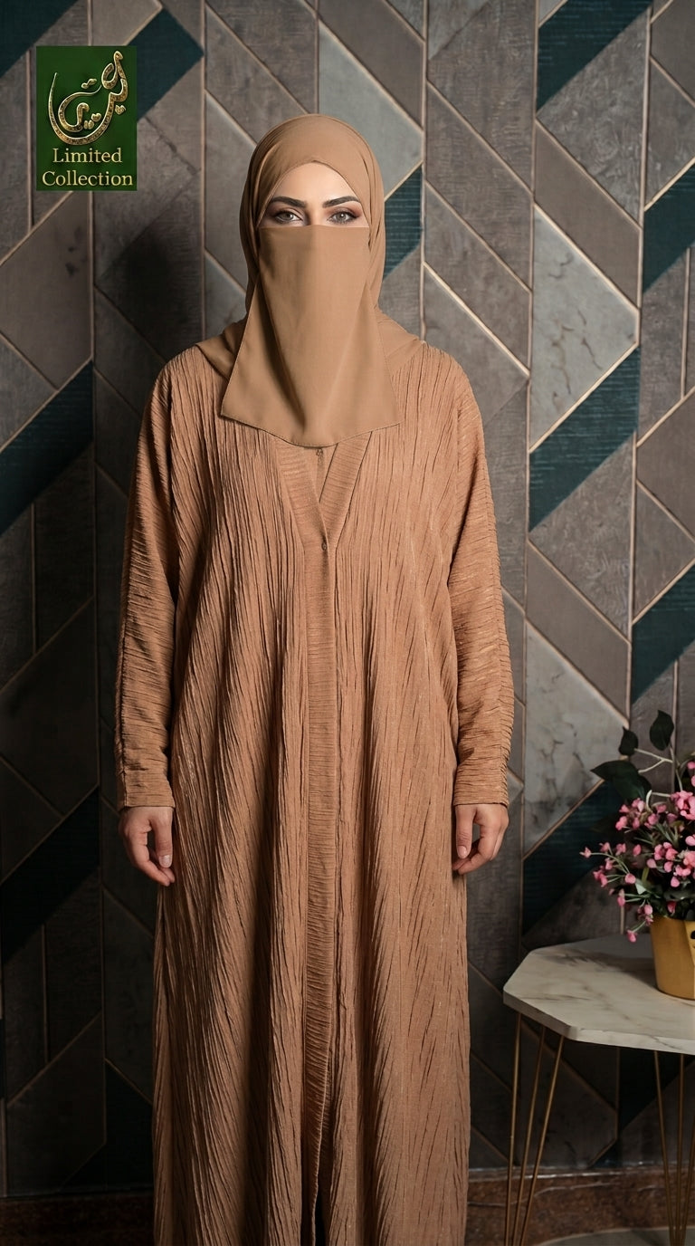 A woman wearing a long, floor-length beige abaya with a matching face-covering hijab stands in front of a geometric tiled wall. A small side table with flowers is visible on the right, and a green 'Limited Collection' logo appears in the top-left corner.