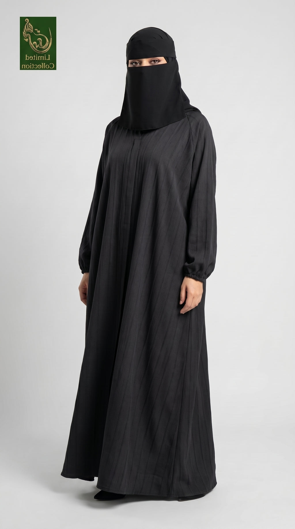 A woman wearing a full-length black abaya and matching black face-covering niqab stands against a light gray studio background. A small green logo appears in the top-left corner.
