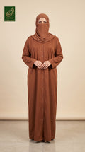 A woman wearing a rust-brown long-sleeve button-front abaya and matching hijab stands against a plain beige studio background. A green 'GCL Limited Collection' logo appears in the top-left corner.