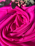 A close-up of draped bright pink fabric arranged in a rose-like spiral, with small dried pink flowers and dark leaves placed at the top edge.