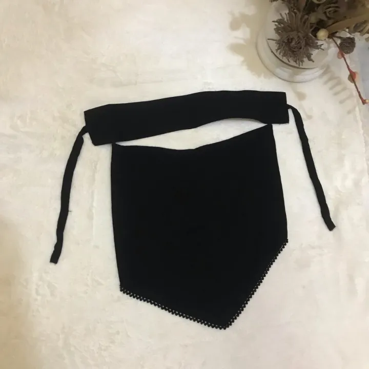 A black knit pet bandana bib with a wide neck strap and tie, laid flat on a textured white surface.