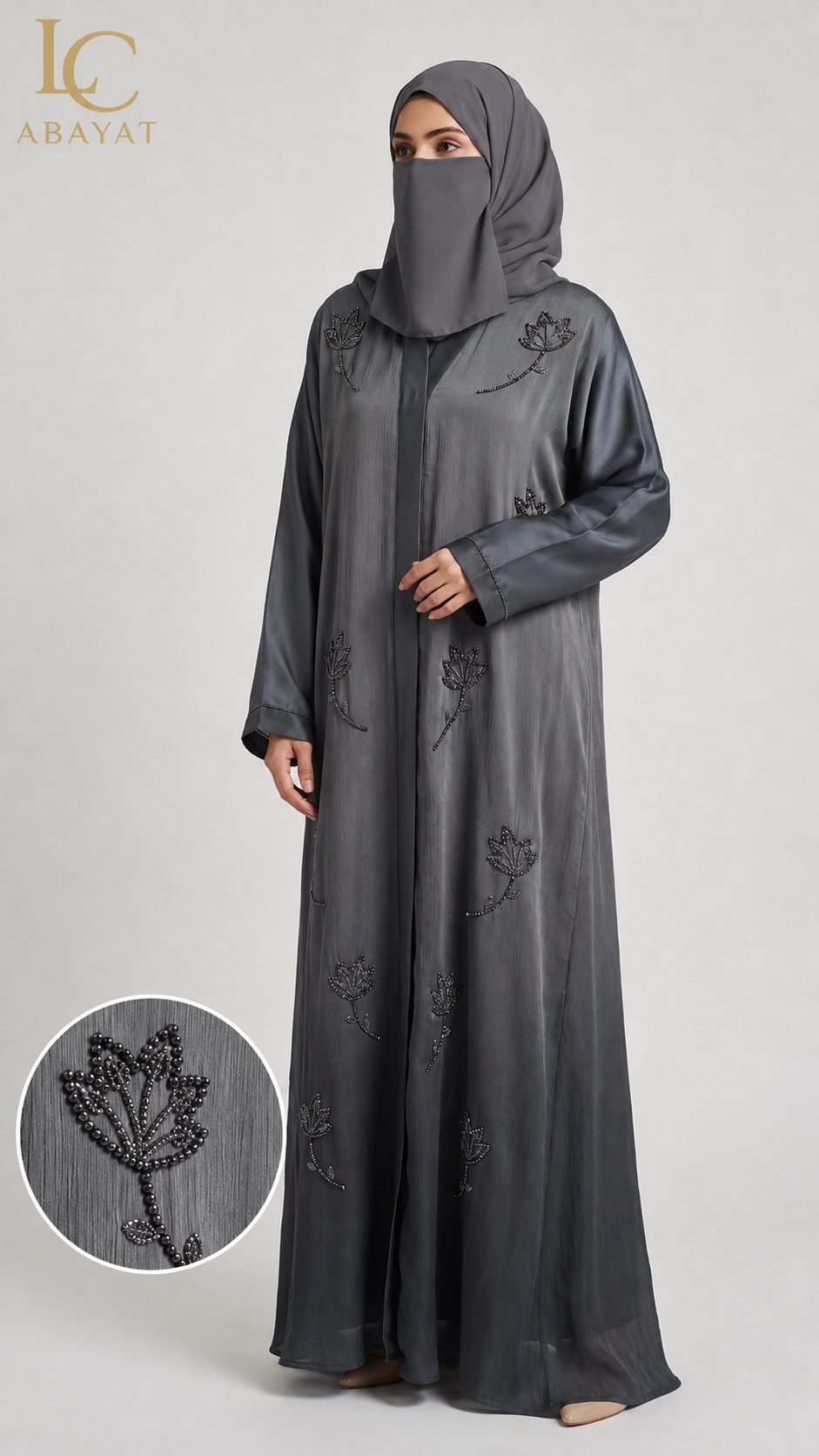 A woman wearing a charcoal abaya and matching hijab with black floral embroidery, shown against a light gray studio background. An inset circle at the bottom left shows a close-up of the embroidered fabric detail.