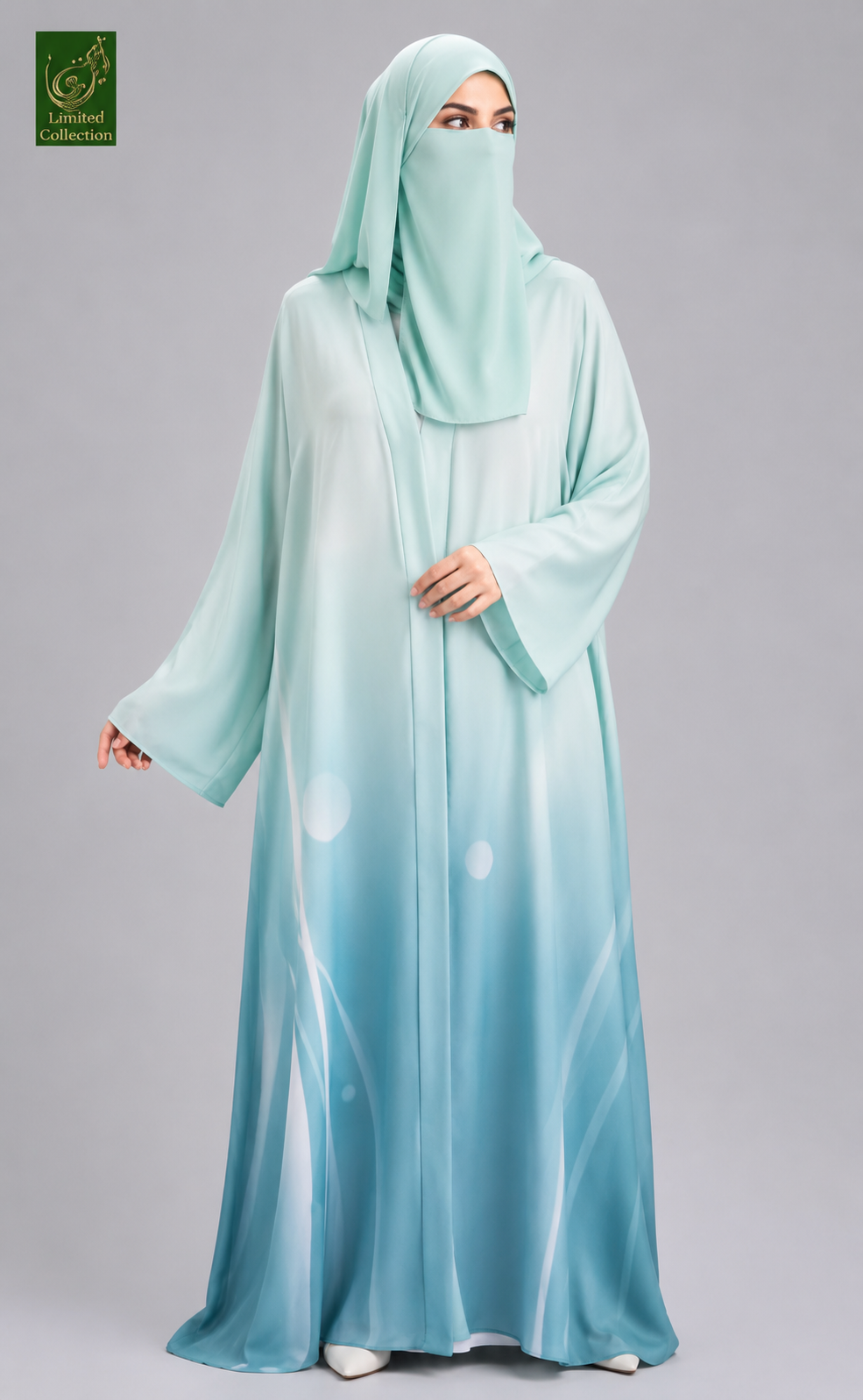 A woman wearing a flowing abaya and matching hijab in a light aqua blue gradient, standing against a solid gray studio background. A green logo for 'The Brand Collection' is visible in the top-left corner.