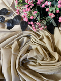 A draped beige fabric scarf or shawl arranged in soft folds, styled with pink flowers and dark leaves on a matching beige fabric background.