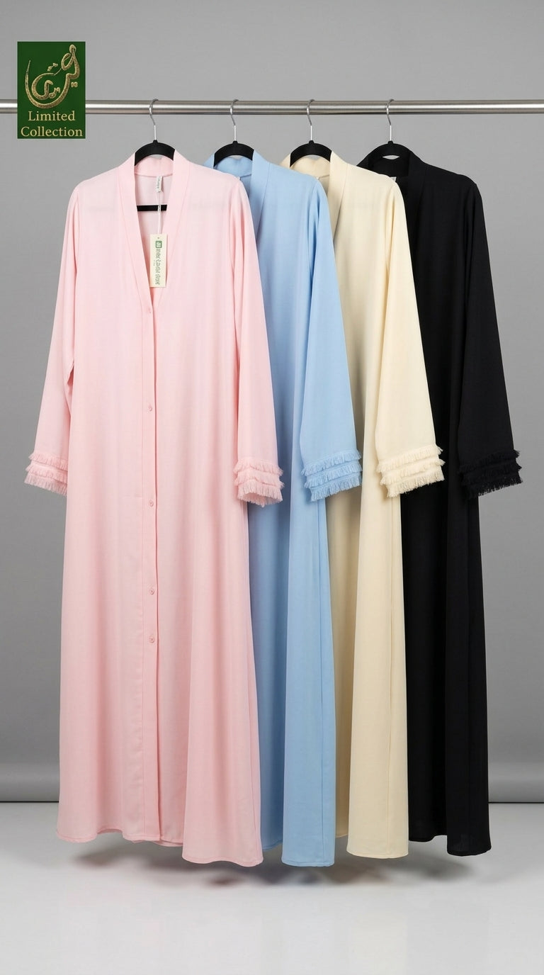 Four long modest abayas hanging on a metal rack against a gray studio background, shown in pink, light blue, cream, and black. The pink abaya is in the foreground and has lace trim at the cuffs, with a green 'GfL Limited Collection' logo in the top left corner.