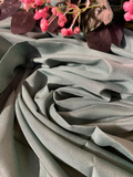 A close-up of draped sage green fabric with soft folds, styled with pink flowers and dark leaves at the top edge.
