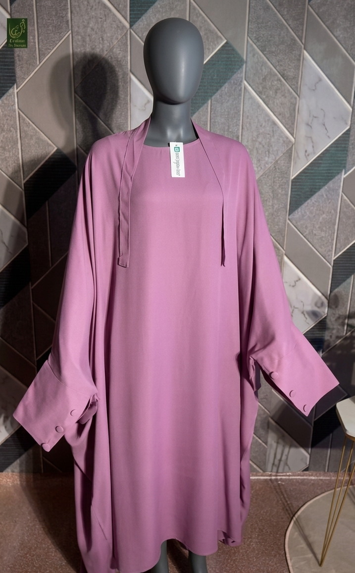 A mauve-pink Jilbab displayed on a dark gray mannequin, set against a geometric patterned wall.