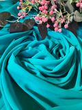 A draped piece of sky blue-green fabric arranged in soft folds, styled with pink flowers and dark leaves at the top against a matching fabric background.