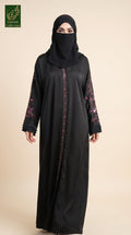 A woman wearing a black abaya with pink floral embroidery on the sleeves and a matching black hijab, standing against a solid beige background. A green 'Abayat Limited Collection' logo is visible in the top left corner.