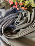 A close-up of draped gray fabric with soft folds, styled with pink flowers and green leaves at the top edge.