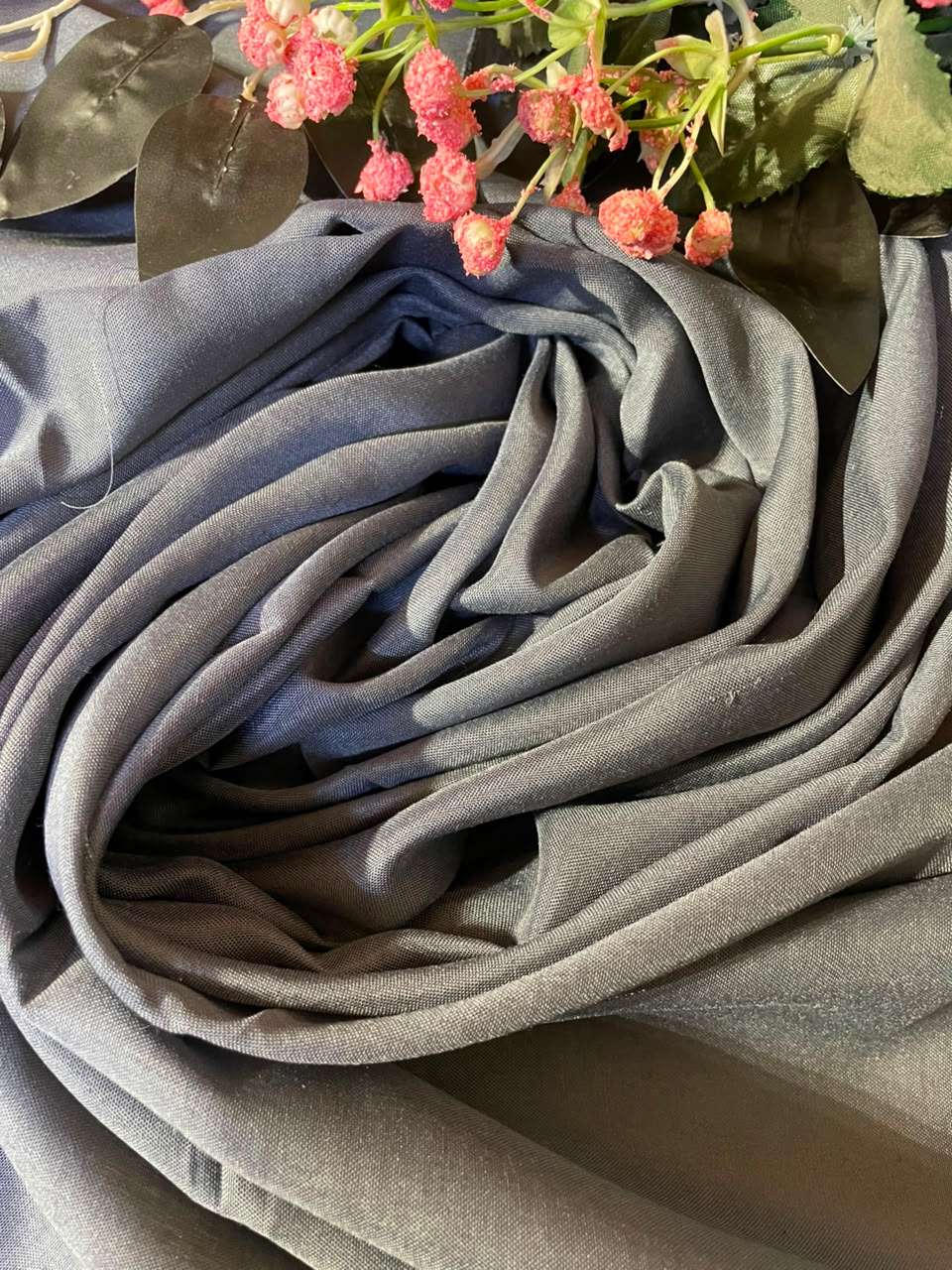 A close-up of draped gray fabric with soft folds, styled with pink flowers and green leaves at the top edge.