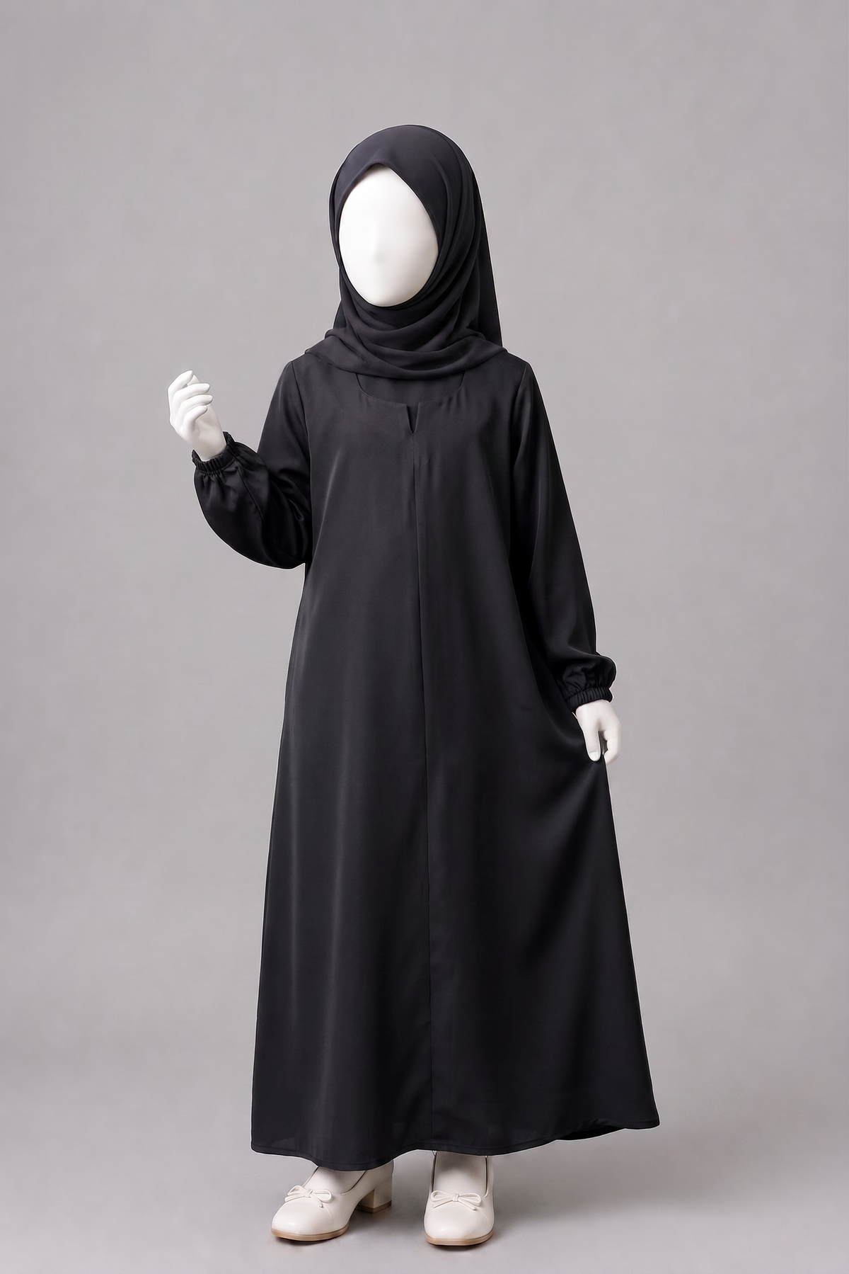 A child's full-body black abaya dress with a matching black hijab, displayed on a white mannequin against a plain gray studio background.