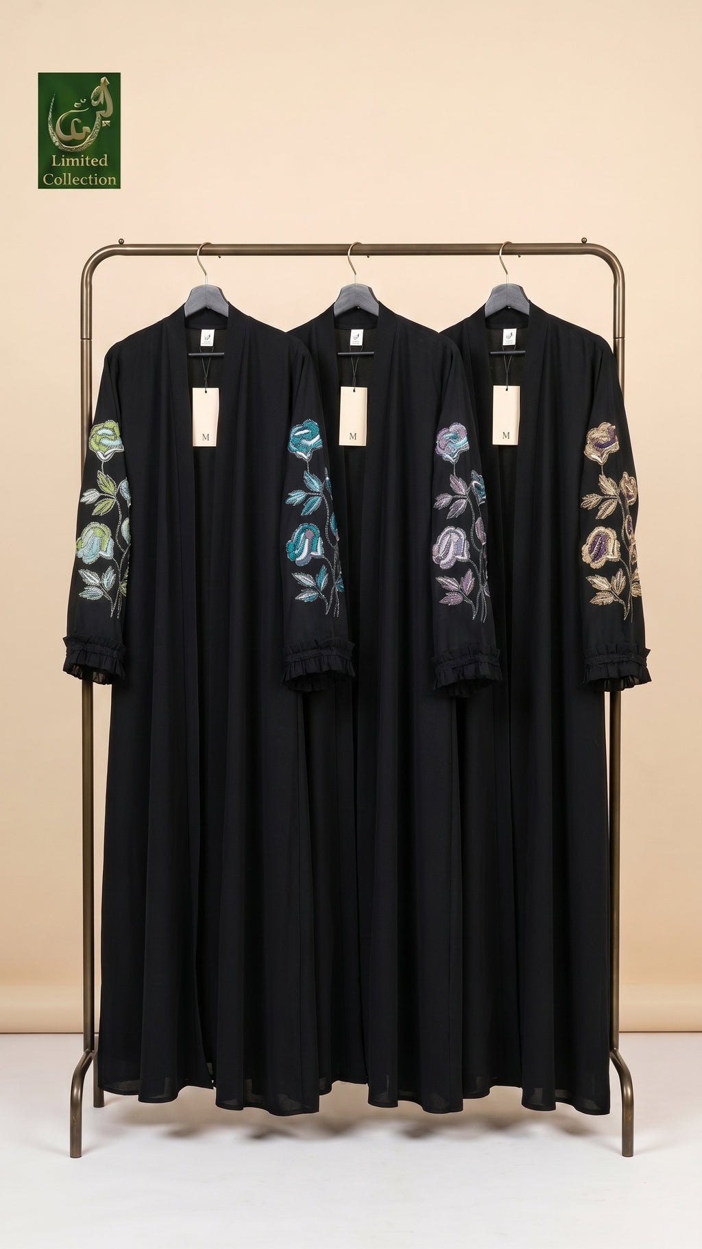 Three black long-sleeve abaya dresses with colorful floral embroidery on the sleeves, hanging on a metal clothing rack against a beige background. A green 'Limited Edition' logo is visible in the top left corner.