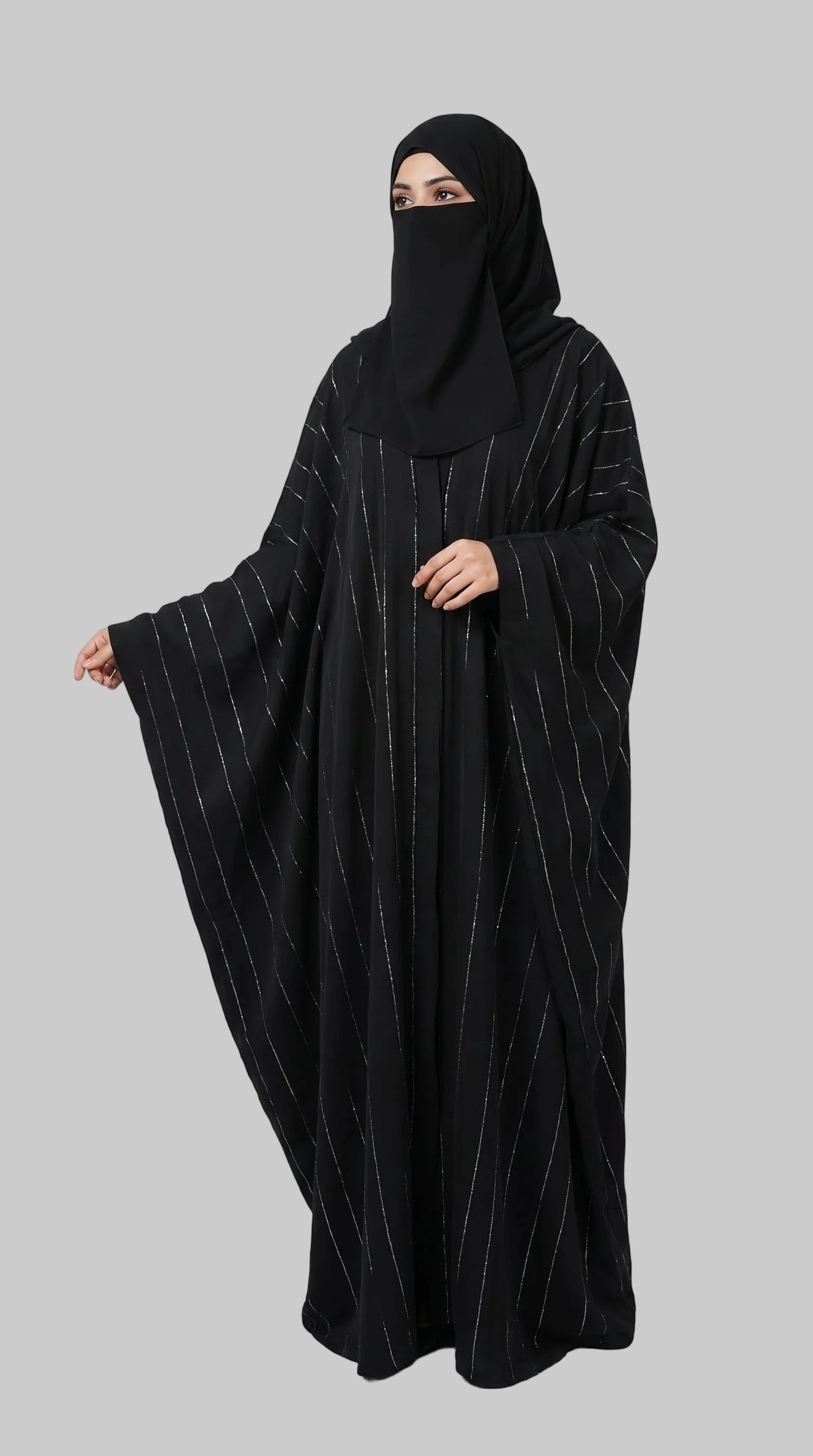 A woman wearing a black abaya with thin vertical metallic stripes and a matching black face covering, standing against a light gray studio background. The brand name LC Abayat  is printed in the top left corner.