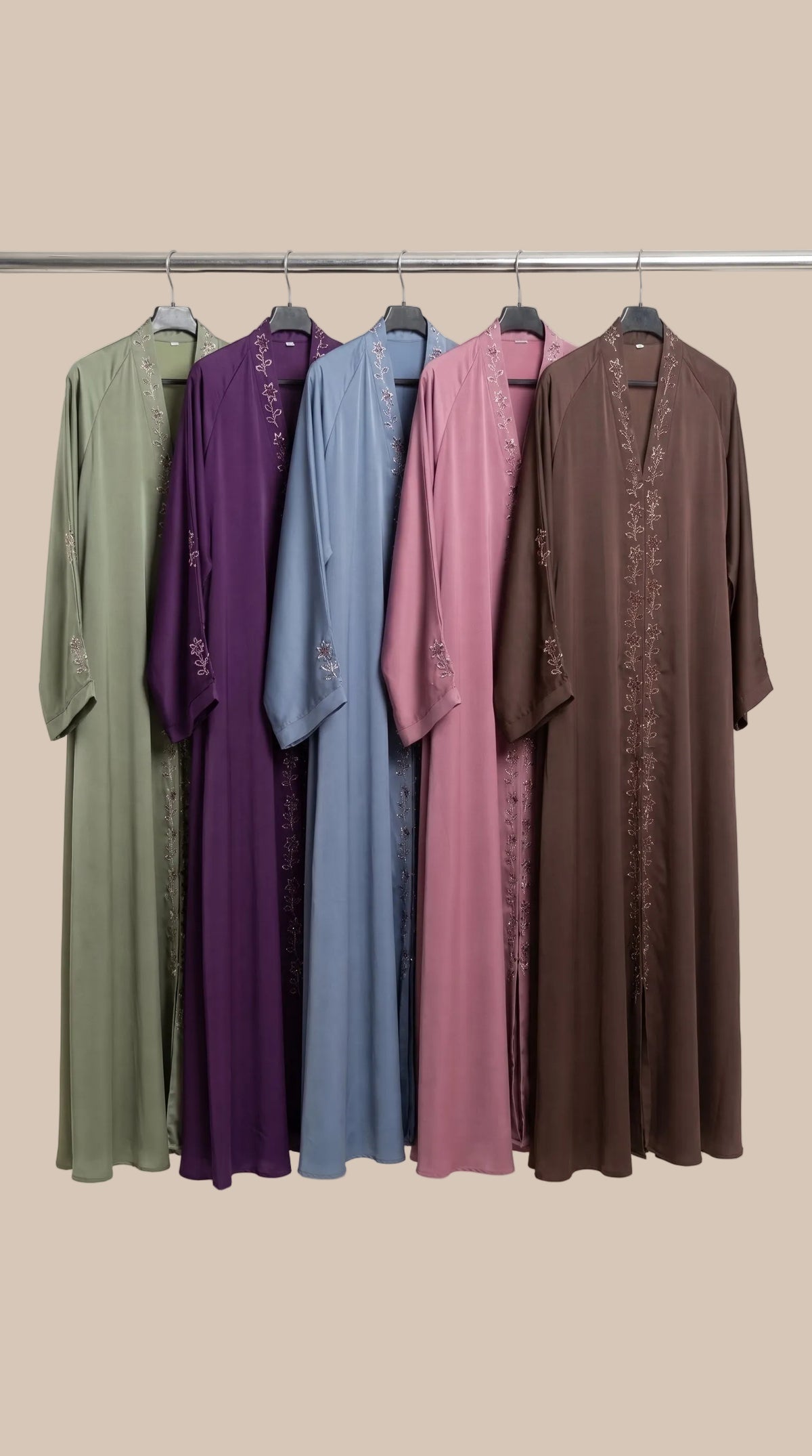 Five long modest abayas hanging on a metal rack against a plain light beige studio background. The garments are shown in different colors: sage green, purple, dusty blue, mauve pink, and dark brown, each with subtle embroidered detailing along the front opening and sleeves.