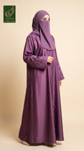 A woman wearing a long, flowing purple abaya with matching embroidered sleeves and a matching hijab, standing against a solid beige studio background. A green 'Limited Collection' logo is visible in the top-left corner.