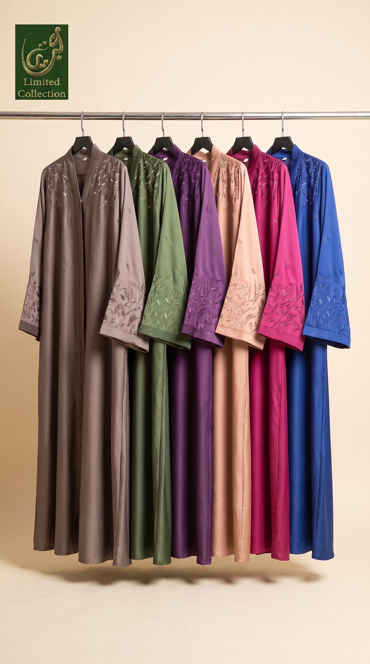 A set of long, loose-fitting abaya dresses hanging on a metal rack against a warm beige background. The collection includes multiple colors: taupe, sage green, plum purple, dusty pink, magenta, and royal blue.