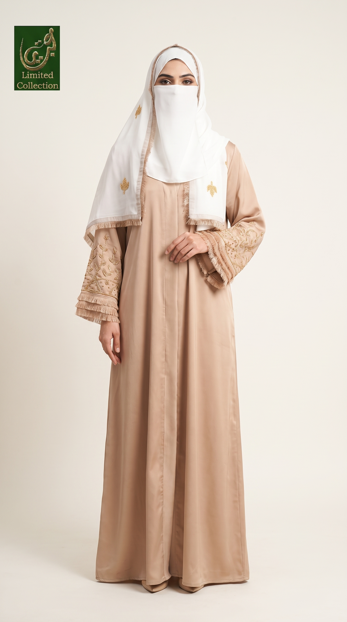 A woman wearing a long beige abaya dress with embroidered sleeves, a white hijab, and a matching headscarf with gold embroidery, standing against a plain light beige studio background. A green 'Limited Collection' logo appears in the top-left corner.